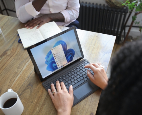 Overhead view of two people at a table working with a Microsoft laptop and notebook